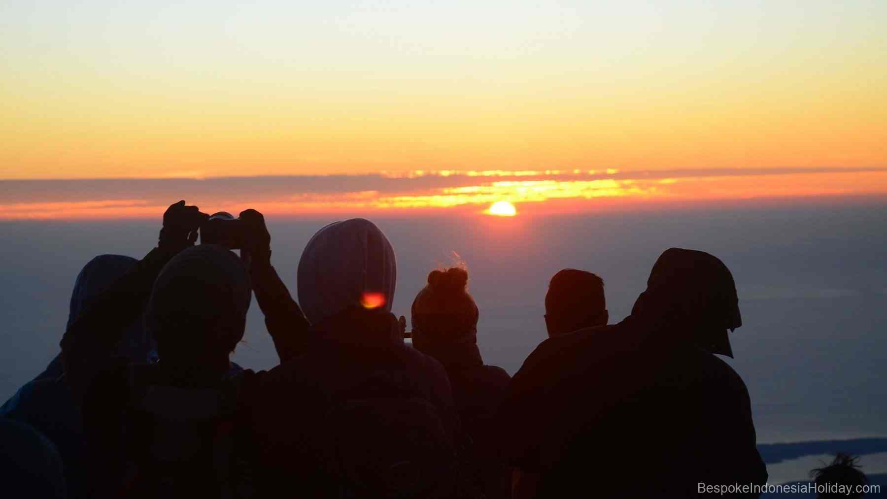 In the foreground 5 dark human figures. The sunrise is orange in front of you. Lombok. Mount Rinjani Trekking Trip | Bespoke Indonesia Holiday.