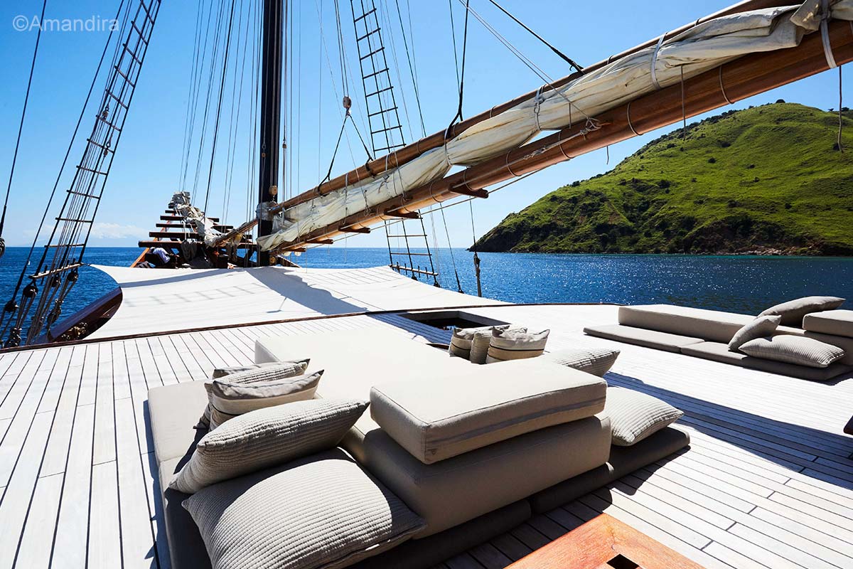 A wooden deck with sun loungers, folded sail, and mast. Amandira. Luxury holidays Indonesia. Luxury Cruise Indonesia. Yacht charter Indonesia. Private cruise Indonesia. Sailing trip Indonesia. Yacht Rental in Indonesia. Bespoke Indonesia Holiday.