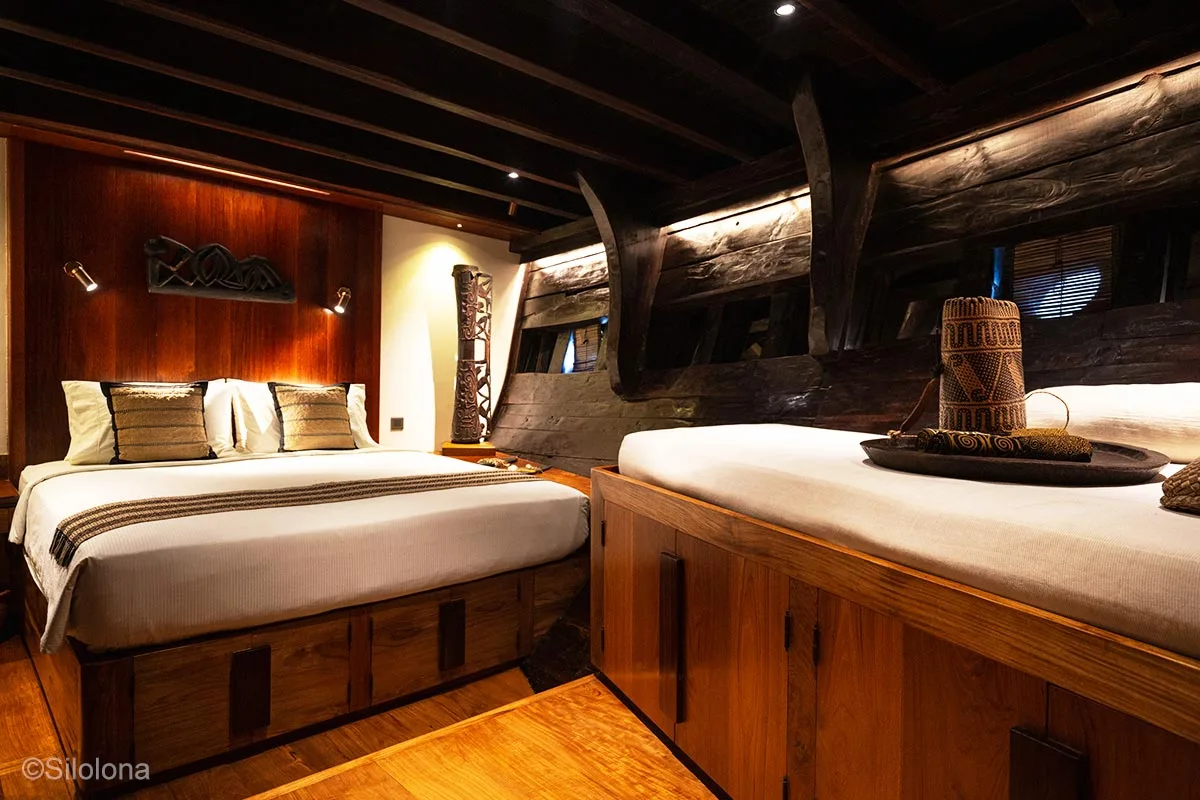 A bedroom utilising dark wood in its interior and dim lighting. Silolona. Silolona Sojourns. Indonesia sailing adventure. Yacht charter Indonesia. Indonesia luxury cruises. Luxury yacht charter Indonesia. Raja Ampat liveaboard. Bespoke Indonesia Holiday.