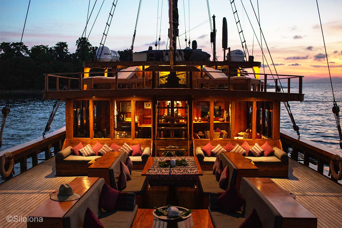 Roofless deck with wooden tables and lounges. Silolona. Silolona Sojourns. Indonesia sailing adventure. Yacht charter Indonesia. Komodo luxury cruises. Luxury yacht charter Komodo. Komodo liveaboard. Bespoke Indonesia Holiday.