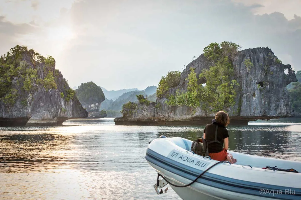 A woman wearing a black shirt and red pants is sitting on a inflatable motor boat looking at the beautiful rock formations in front of her. Aqua Blu. Aqua Blu Yacht. Luxury holidays Indonesia. Luxury Cruise Indonesia. Luxury cruise Raja Ampat. Luxury cruise komodo. Yacht charter Raja Ampat. Yacht charter Indonesia. Yacht charter Komodo. Private cruise Indonesia. Sailing trip Indonesia. Yacht Rental in Indonesia. Yacht charter for a big family in Indonesia. Yacht charter for a big group in Indonesia. Bespoke Indonesia Holiday.