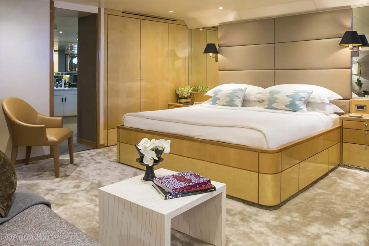 A beautiful king-sized bed with bedside table on each side, wardrobe on the left side, beautiful brown chair that matches the interior, grey couch, and white table adorned with orchids and books. Aqua Blu. Aqua Blu Yacht. Luxury holidays Indonesia. Luxury Cruise Indonesia. Luxury cruise Raja Ampat. Luxury cruise komodo. Yacht charter Raja Ampat. Yacht charter Indonesia. Yacht charter Komodo. Private cruise Indonesia. Sailing trip Indonesia. Yacht Rental in Indonesia. Yacht charter for a big family in Indonesia. Yacht charter for a big group in Indonesia. Bespoke Indonesia Holiday.