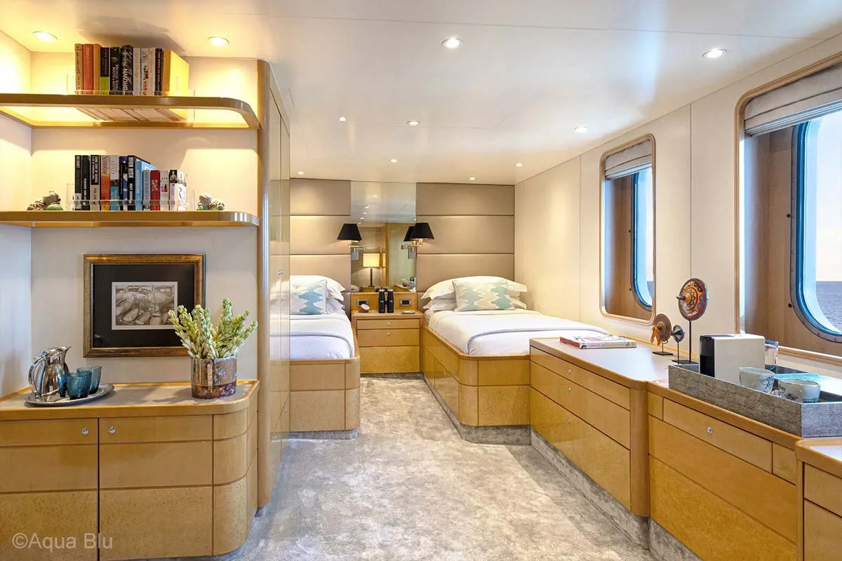 A beautiful twin cabin with books, glasses, and flower arrangement on the left, more glasses on top of drawer table on the right side, and ship windows. Aqua Blu. Aqua Blu Yacht. Luxury holidays Indonesia. Luxury Cruise Indonesia. Luxury cruise Raja Ampat. Luxury cruise komodo. Yacht charter Raja Ampat. Yacht charter Indonesia. Yacht charter Komodo. Private cruise Indonesia. Sailing trip Indonesia. Yacht Rental in Indonesia. Yacht charter for a big family in Indonesia. Yacht charter for a big group in Indonesia. Bespoke Indonesia Holiday.