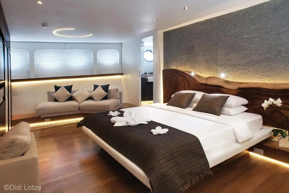 An airy room features a king-sized bed, toilet, sofas, and beautiful flower decorations and towel animal art. Pelagian Dive Yacht. Wakatobi diving. Pelagian Liveaboard. Wakatobi Resort. Wakatobi. Wakatobi National Park. Luxury liveaboard Indonesia. Luxury liveaboard Wakatobi. Diving expeditions Indonesia.Reef diving Indonesia. Indonesia Liveaboard trip. Yacht charter Indonesia. Boat rental Indonesia. Diving trip in Indonesia. Luxury diving trip. Bespoke Indonesia Holiday.