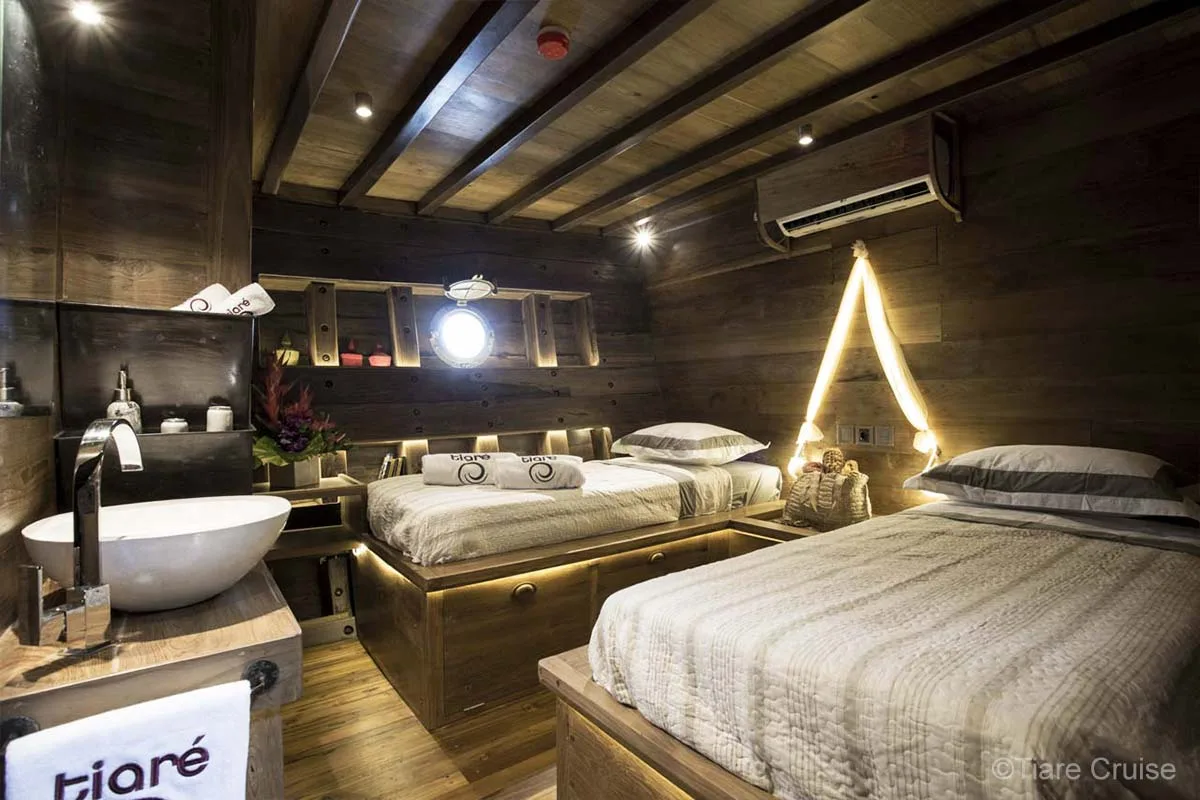 A wooden cabin with twin beds, air-conditioning, a porthole, minibar, and washbasin. Tiare Cruise. Luxury liveaboard Indonesia. Luxury liveaboard Raja Ampat. Luxury liveaboard Komodo. Diving expeditions Indonesia. Liveaboard tours Indonesia. Yacht charter Indonesia. Yacht charter komodo. Yacht rental Indonesia. Luxury Cruise Indonesia. Luxury Cruise Komodo. Luxury Cruise Raja Ampat. Bespoke Indonesia Holiday.