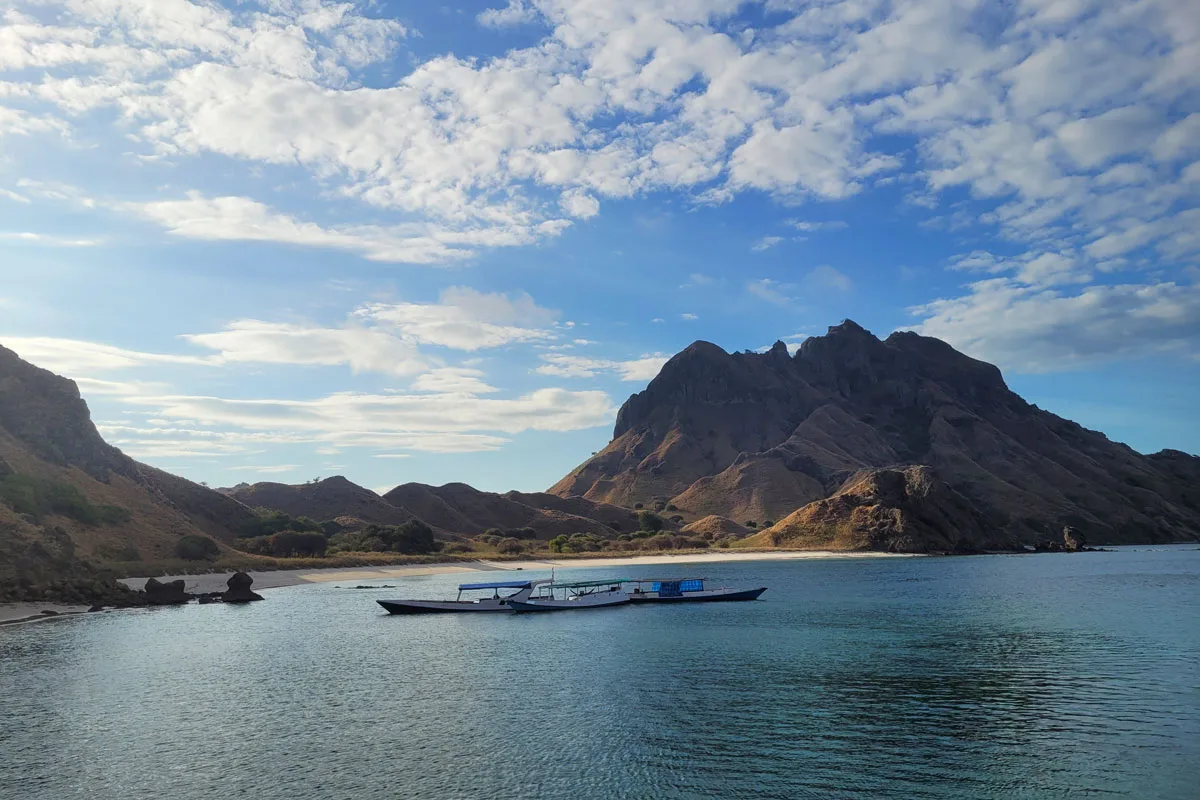 There are two small boats anchoring by an island with steep hillsides covered in dry savanna and encompassed by white sand beach. Padar Island. Komodo Island National Park. Sailing Destinations in Indonesia. Top Sailing Destinations in Indonesia. Komodo Liveaboard. Liveaboard Indonesia. Private Cruise Komodo. Bespoke Indonesia Holiday.